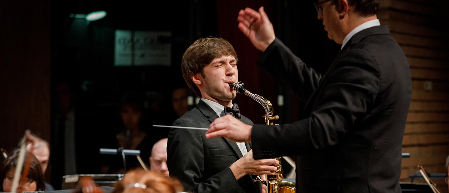 Young man playing saxophone solo with a symphony orchestra